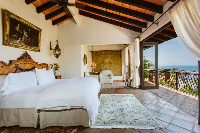 Angel's View Suite at Hacienda San Angel features a beautiful antique wooden bed, white bedding, a sitting area adorned with antique art and tapestries, and a terrace overlooking the stunning Bandera's Bay.