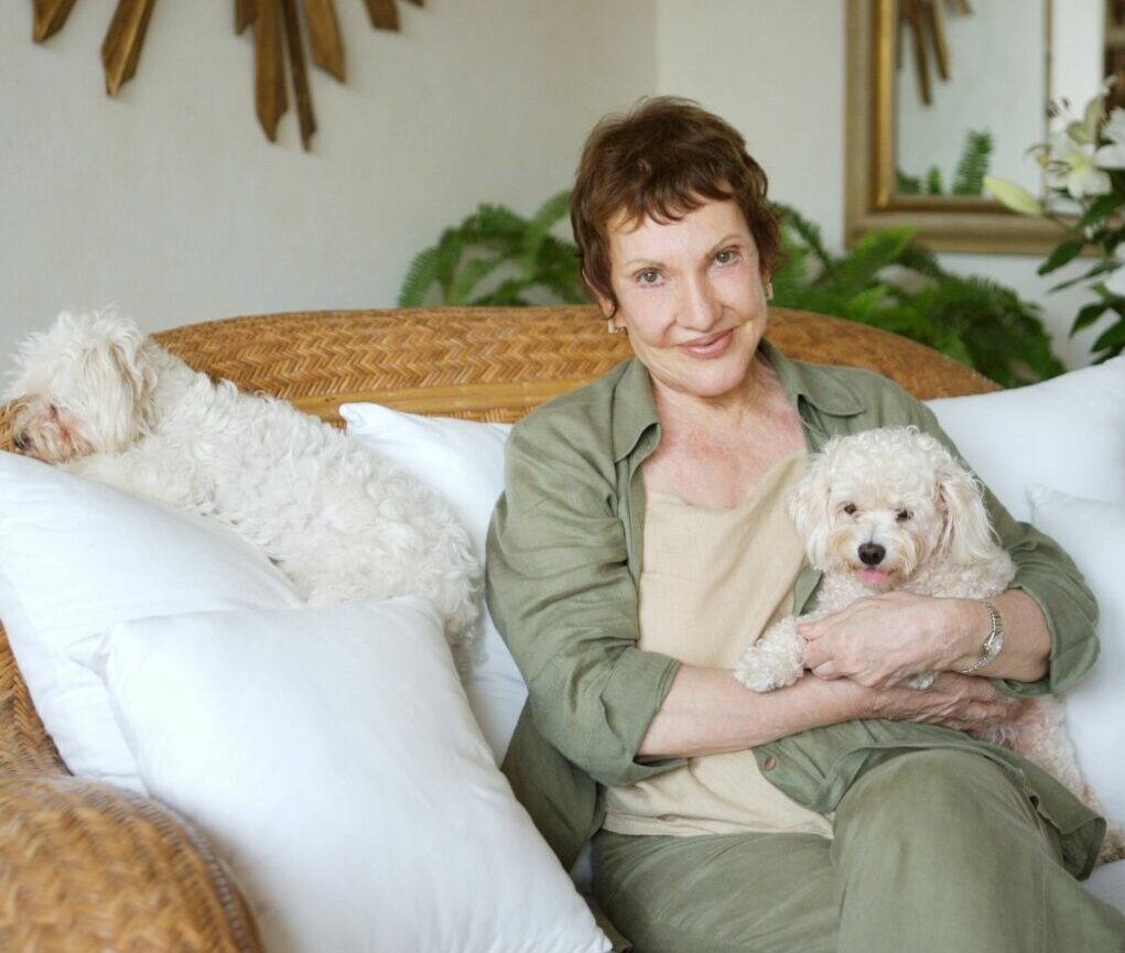La Doña sitting on couch with two of her little white dogs.
