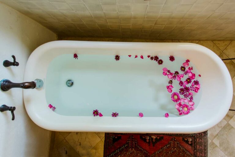 Birdseye view of clawfoot tub with bright pink flowers floating in water.