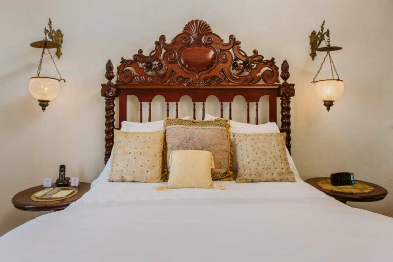 Close-up of beautiful carved wooden bed with white bedding and antique style decorative pillows.