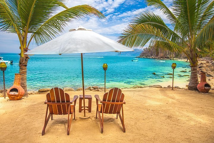 Las Caleta's private beach and property of the late John Huston sits two beach chairs, a white umbrella with palm trees and tiki torches.