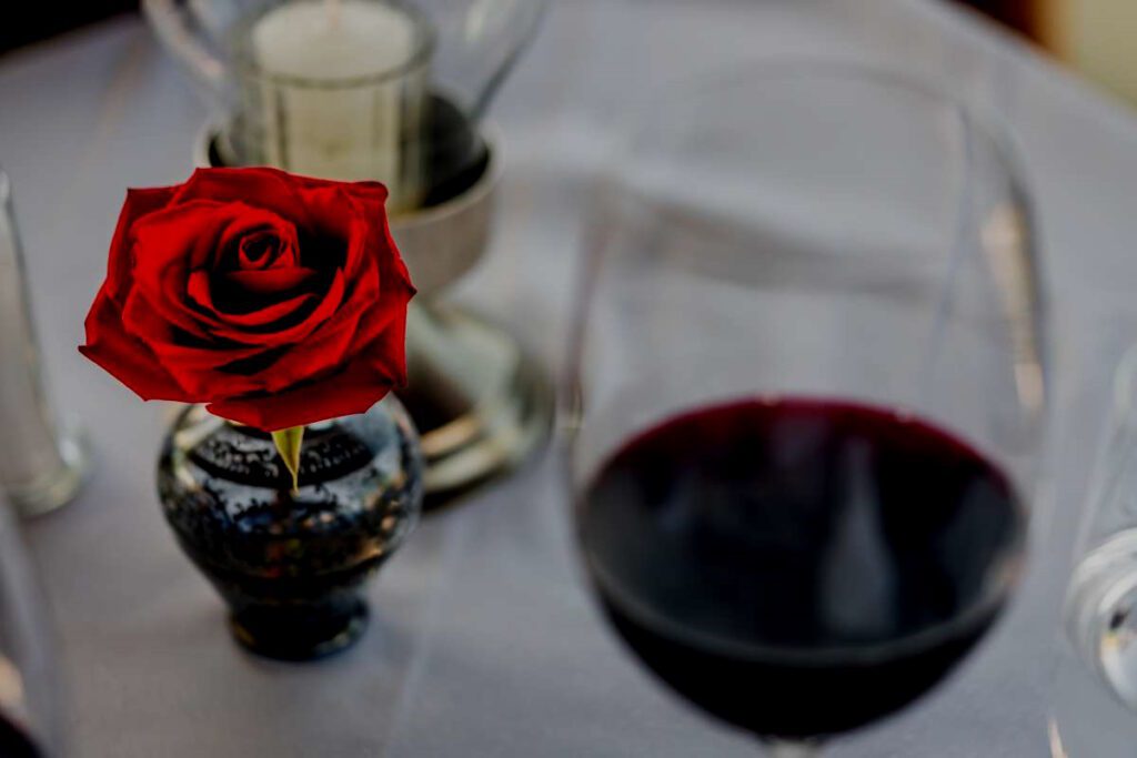 Close-up view of a sophisticated table arrangement featuring a candle, a single red rose, and a glass of red wine.