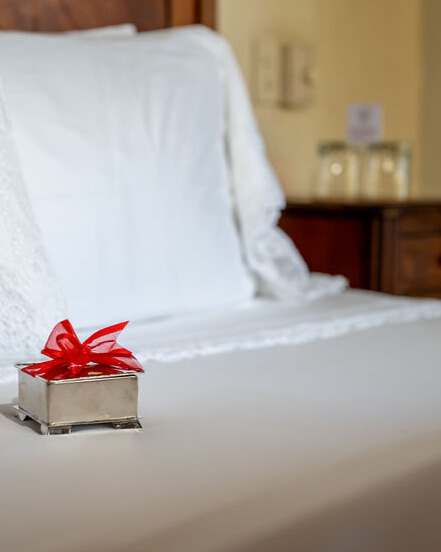 Silver box of chocolates with a red ribbon on top, placed elegantly on stunning white bedding.